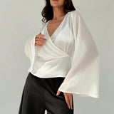 Blusa blanca de mujer con cuello en V profundo transparente, mangas largas abocinadas y munequeras con cintura suelta